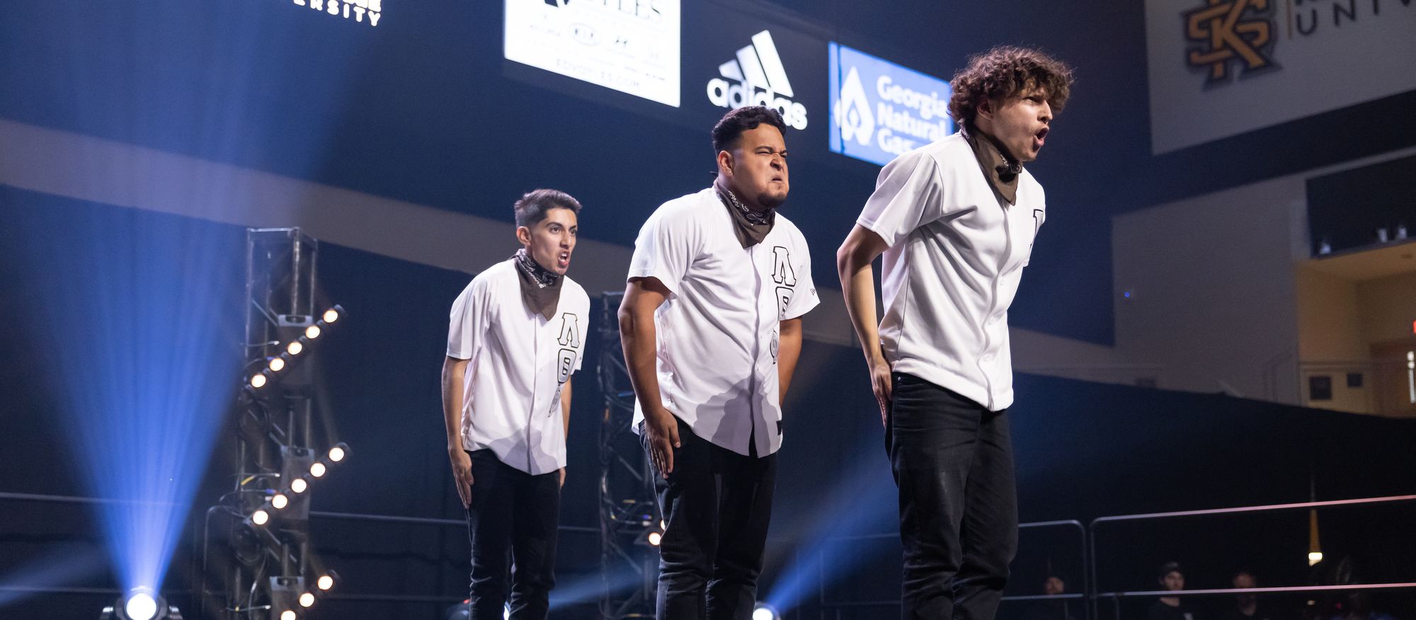 Three brothers performing on stage in white jerseys under blue stage lighting.