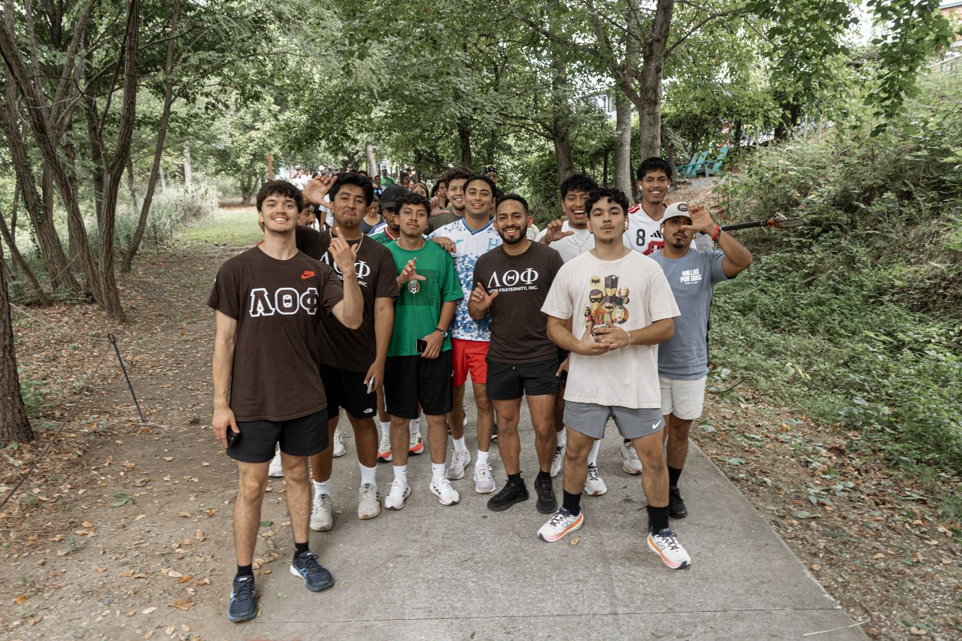 Brothers walking together down a shaded stretch of the trail, throwing the fraternity hand sign.