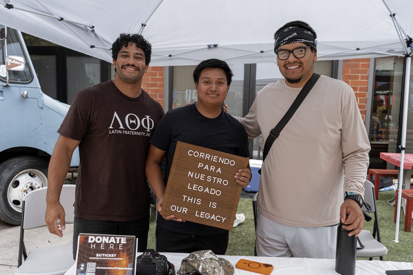 Three volunteers behind the donation table holding the letterboard, next to a sign reading Donate Here, five dollars a ticket.