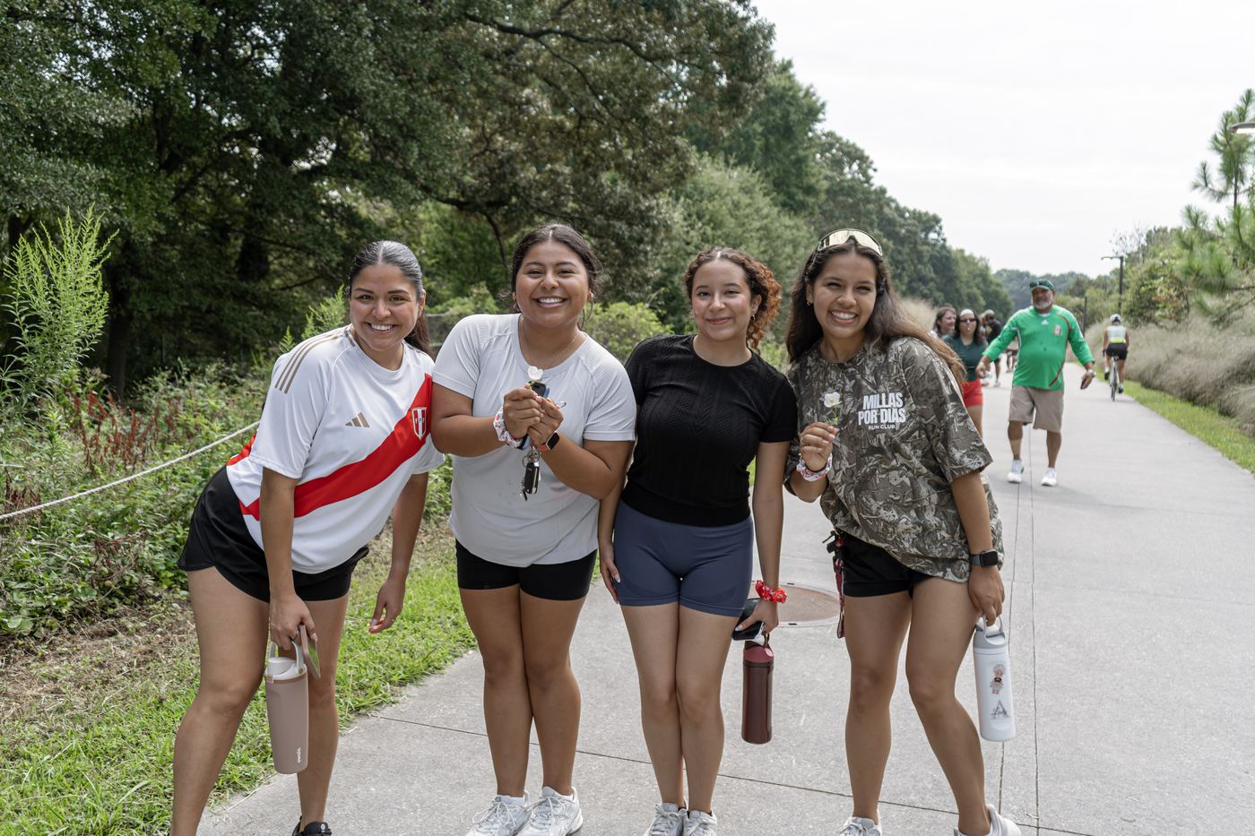 Four runners stopping on the trail to pose, each holding a small white flower.