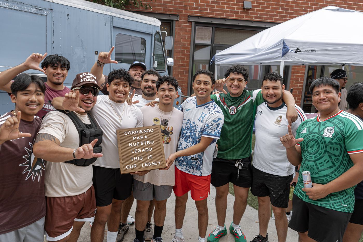 A dozen runners crowded together in front of a food truck, throwing the fraternity hand sign around the letterboard.