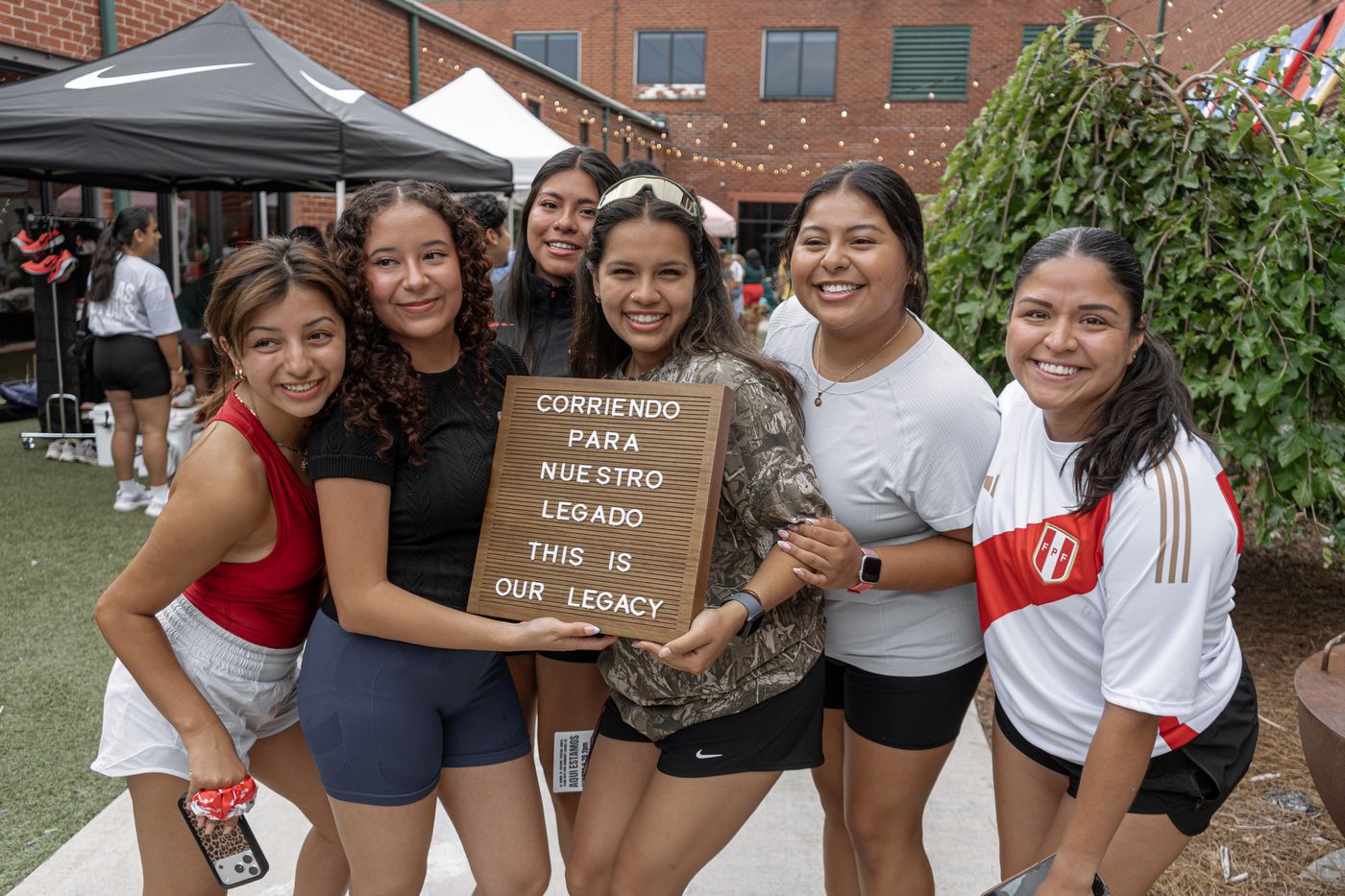 Six runners leaning in together around the Corriendo para Nuestro Legado letterboard.