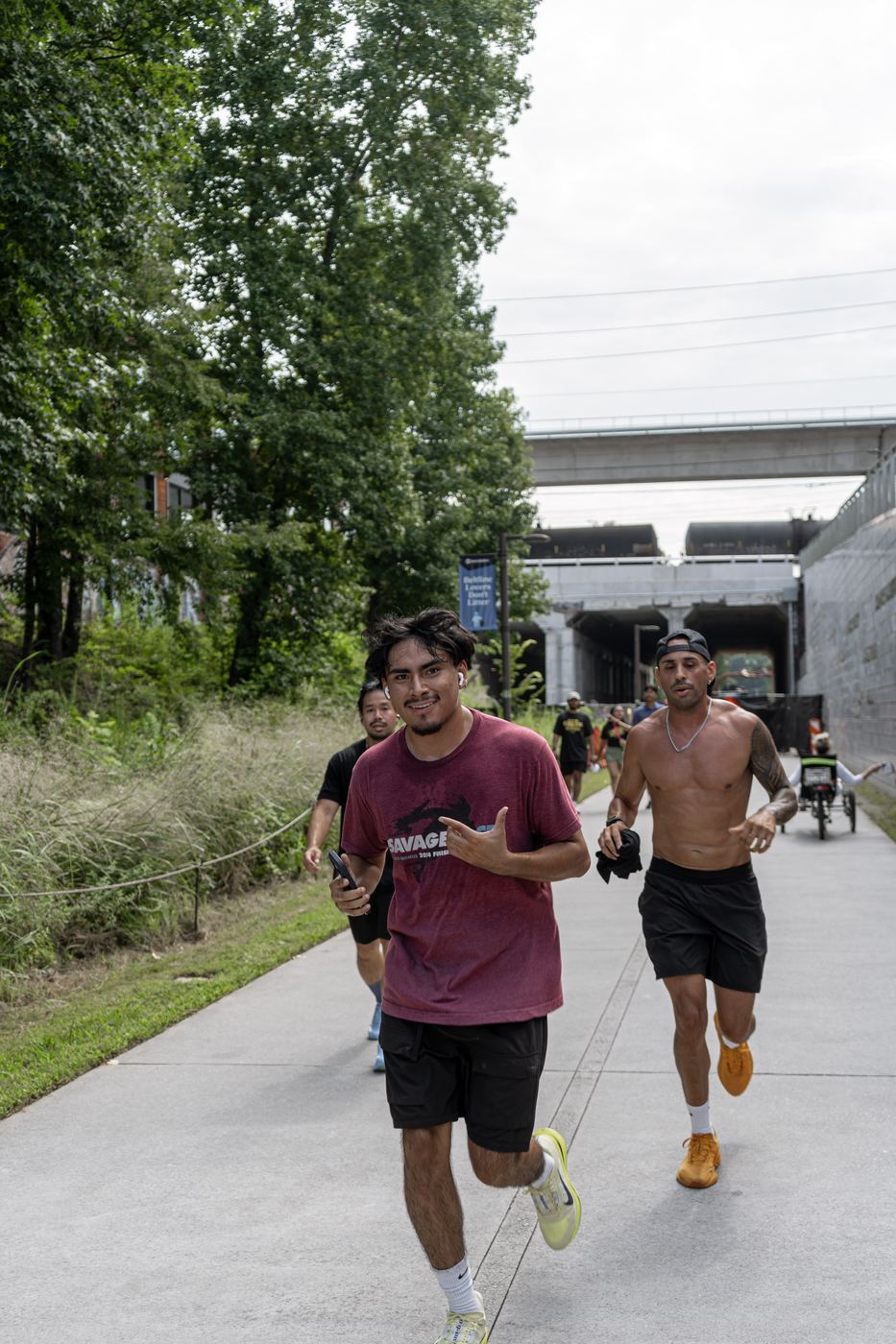 Runners strung out along the trail under the rail bridge, the leaders closest to the camera.