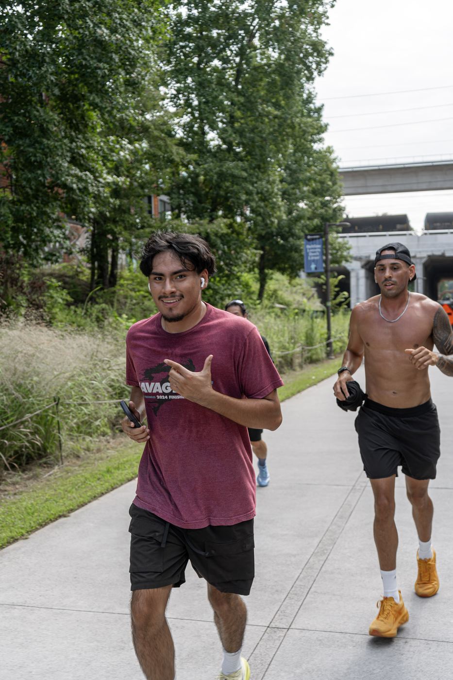 Two runners coming up the trail toward the camera with a rail bridge behind them.