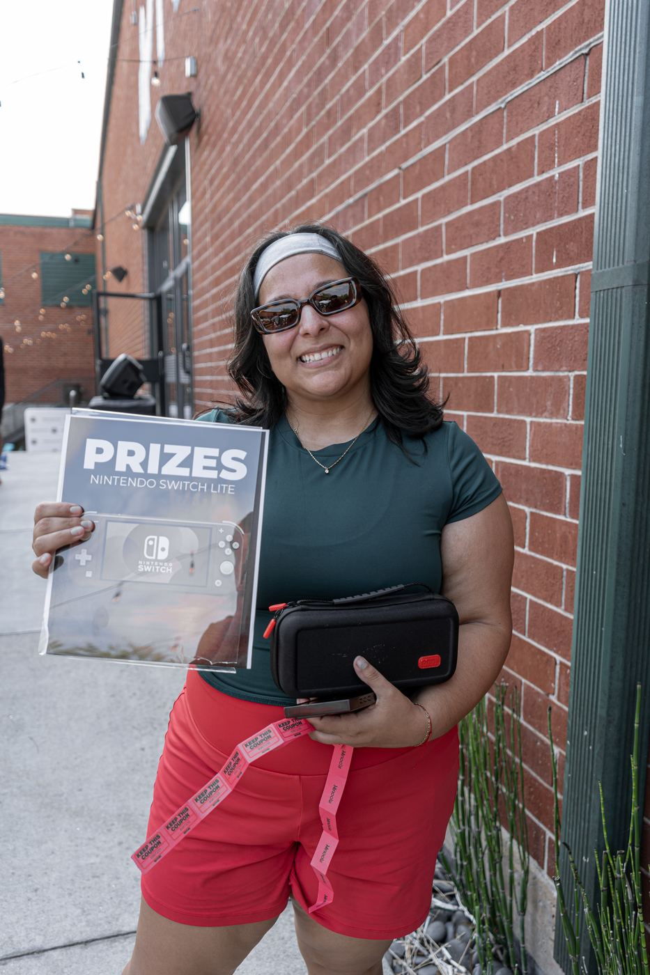 A raffle winner holding the Nintendo Switch Lite prize and its case, raffle tickets still tucked into a pocket.