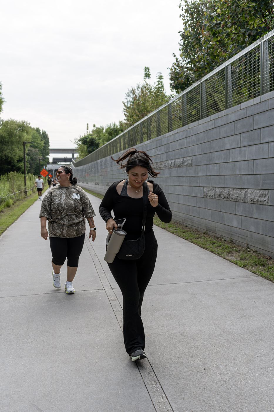 Two walkers making their way along the trail beside a grey block retaining wall.