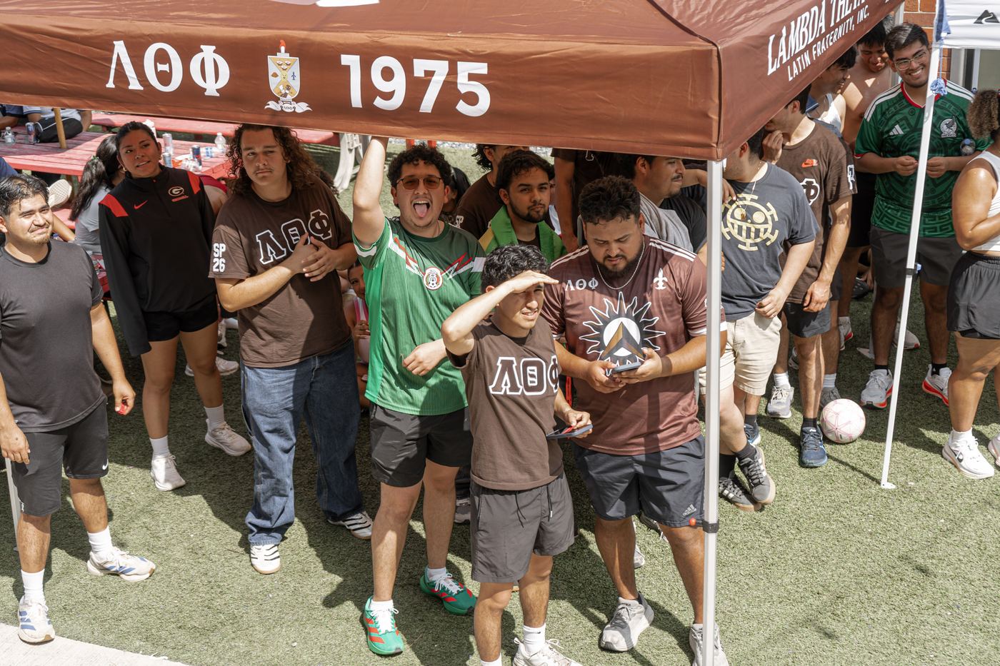 Brothers packed under the Lambda Theta Phi 1975 tent, waiting on the raffle drawing.